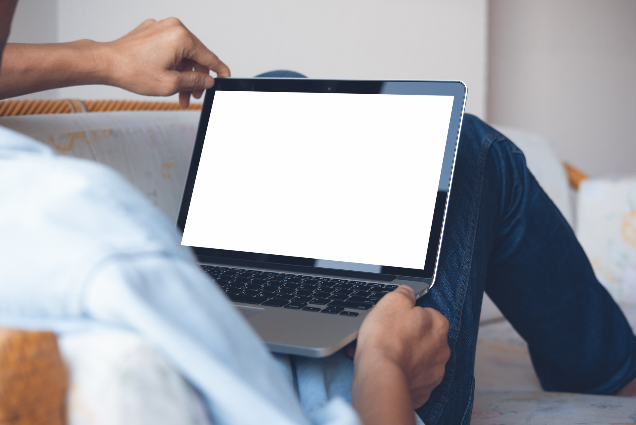 Mockup image of casual man leaning on sofa, relax using blank screen laptop computer at home or hotel room, over shoulder view, close up