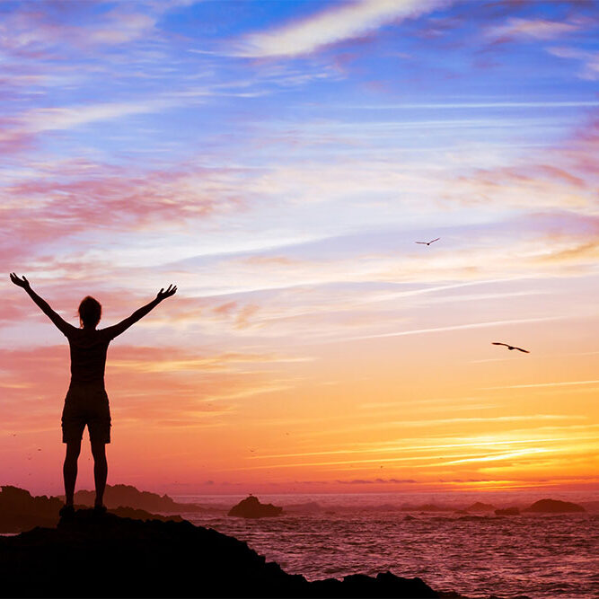 silhouette of woman with raised hands on beautiful sunset background