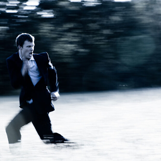 A gritty motion blurred image of a young banker running through a field screaming.